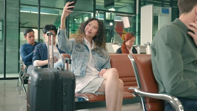 Enjoy travel vacation alone. Happy Asian young beautiful woman curly hair taking selfie by smartphone at airport terminal hall while waiting for her flight, tourist girl in international airport