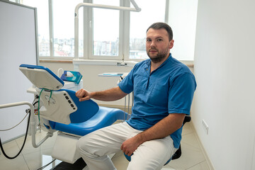 handsome male professional dentist sitting in his own dental office in medical clothes.