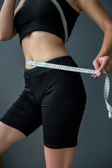 waist view of a sporty woman measuring her size with a tape.