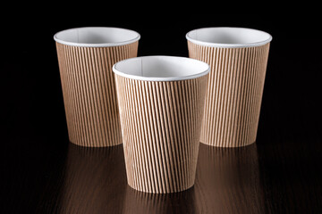 Three disposable paper cups with a corrugated surface on a black background. Selective focus. Angle...