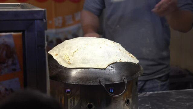 Professional and skilful chef flipping dough with fanning motion and flip side of rumali roti on hot wok at famous street night market in Douliu city, Yunlin county, Taiwan.