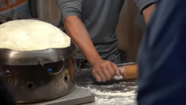 Professional chef roll the dough with rolling pin and flip the side of rumali roti cooking on the hot wok at famous street night market in Douliu city, Yunlin county, Taiwan.