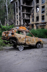 Obraz na płótnie Canvas Burned car after the terror attacks a result of the Russian invasion of Ukraine the backdrop of a war-torn house. Exploded car. Damage auto of civilians. War in Ukraine. War crimes.