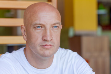 Portrait handsome bald man with blue eyes in a white t-shirt with a pensive look, closeup on the...