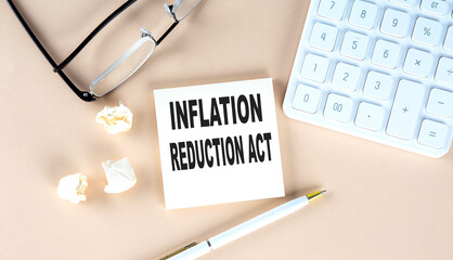 Inflation Reduction Act text on sticky with pen ,calculator and glasses on a beige background