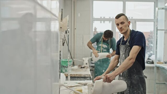 Portrait of modern young adult Caucasian man wearing apron forming plaster cast in prosthetic production workshop looking at camera