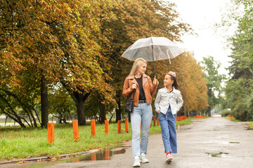 Obraz premium Mom holds a transparent umbrella from which fall autumn leaves. Daughter and mother laugh. Happy mom and little daughter having fun in autumn park.