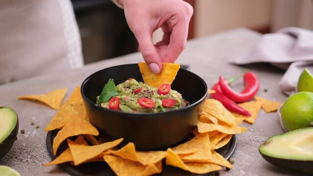 woman dips nachos chips to freshly made guacamole dip sauce in marble bowl mortar