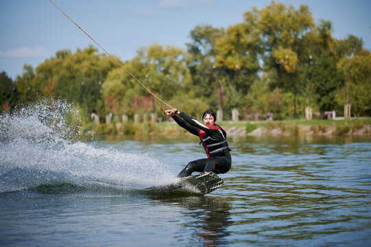 Wakeboarder surfing on lake. Young man surfer having fun wakeboarding in the cable park. Water sport, outdoor activity concept.