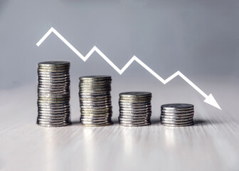 Stacks of coins on the table, decreasing income with a graphic arrow.