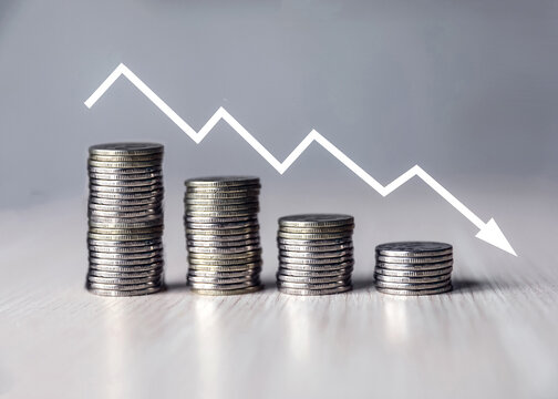 Stacks of coins on the table, decreasing income with a graphic arrow.