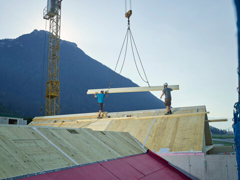 Carpenters installing roof with help of crane at construction site