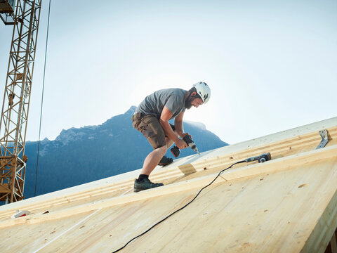Carpenter working with drill on roof at construction site