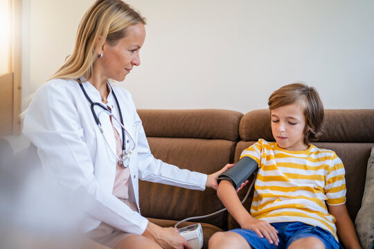Female doctor taking boy's blood pressure on couch at home