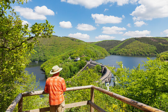 Senior man wearing hat looking at Urft Dam on sunny day, Eifel National Park, Germany