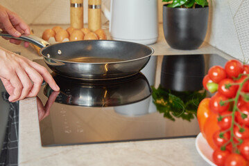 Modern kitchen appliance, Woman hand turn on induction stove with steel frying pan, Finger touching...