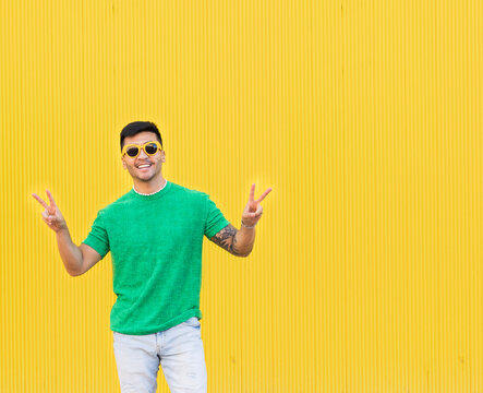 Happy young man gesturing peace sign in front of yellow wall