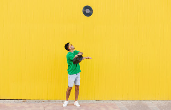 Young man juggling vinyl records in front of yellow wall