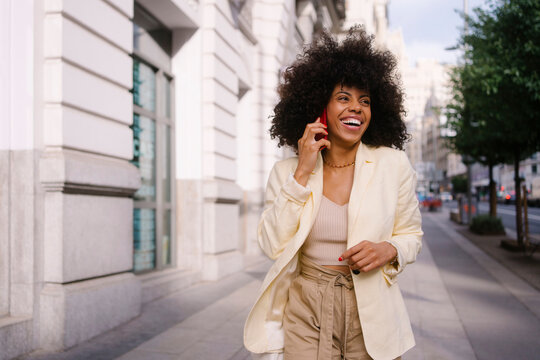 Happy woman talking on smart phone walking at sidewalk
