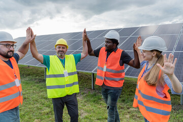 Smiling engineers high-fiving and standing in front of solar panels at field