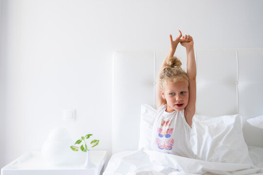 Little girl stretching arms sitting in bed
