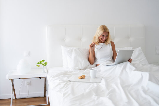 Smiling woman working on laptop by breakfast on bed