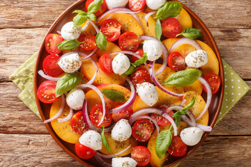 Summer peach Caprese salad with mozzarella and cherry tomatoes close-up in a plate on a wooden table. Horizontal top view from above