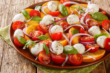 Summer peach Caprese salad with mozzarella and cherry tomatoes close-up in a plate on a wooden table. Horizontal