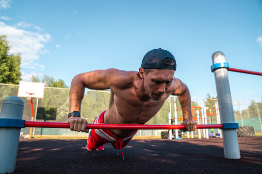 Fit athlete practicing push-ups on horizontal bar at park