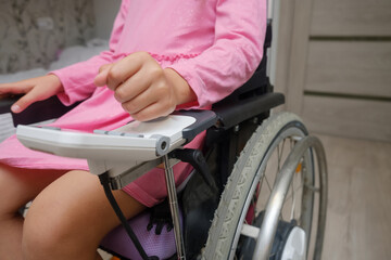 baby girl in a dress sitting on an electric wheelchair indoors. close-up photo of electric wheelchair joystick	