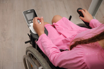baby girl in a dress sitting on an electric wheelchair indoors. close-up photo of electric wheelchair joystick	