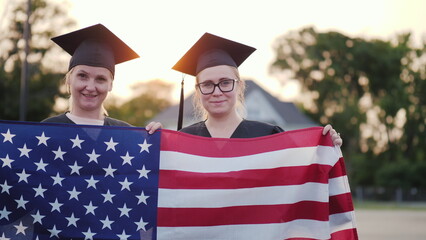 Two college graduates in gowns and caps with the American flag