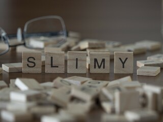 Slimy word or concept represented by wooden letter tiles on a wooden table with glasses and a book