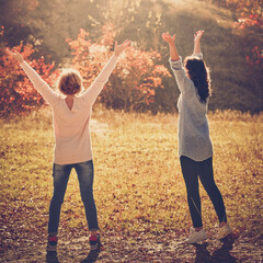 Two happy female friends enjoying golden autumn fall on sunny day