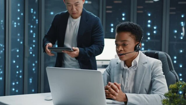 Close up asian man of tech specialists communicating with african amercan woman in headphone at server room. Professional IT service managers developing software. Call center
