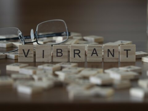 Vibrant word or concept represented by wooden letter tiles on a wooden table with glasses and a book