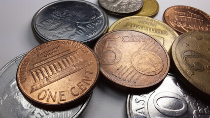 1 Dollar cent coin, with the writing “E Pluribus Unum”, and a 5 Euro cents coin, together with a collection of various old coins on a white background.