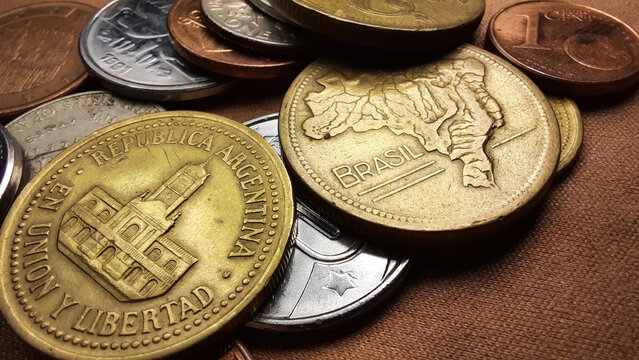 Golden Peso coin, with the image of the Cabildo of Buenos Aires building, and a Golden Cruzeiro coin, with Brazil’s map, together with a collection of various old coins on a brown background.