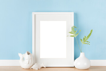 Elegant vertical white transparent picture frame with matte poster mockup and Japanese decoration in front of pastel blue wall.