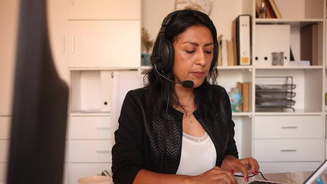 Portrait of experienced female customer support phone operator with headphones during work in call center