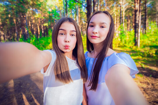 Two teen girls make selfie in the forest. Summer sunny day