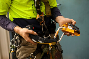 Rope access inspector inspecting self controlled stop a fall descent safety 
device with absorbing lanyard attached  prior to use clipping into chest harness loop  
 - obrazy, fototapety, plakaty