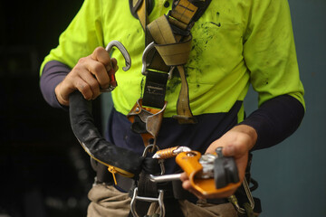 Rope access inspector clipping locking Karabiner into front of full body safety abseiling harness...