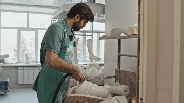 Young adult Caucasian man with beard on face wearing apron working on artificial leg socket cast in workshop