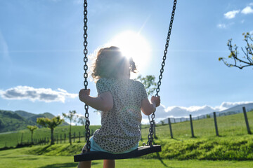 little caucasian girl alone and sad on the swing in the park - playground- concept of shyness,...