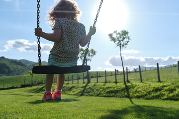 little caucasian girl alone and sad on the swing in the park - playground- concept of shyness,...