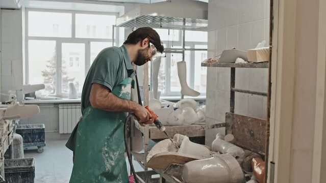 Professional craftsman wearing apron and protective eyeglasses drilling hole in plaster cast for prosthetic limb socket