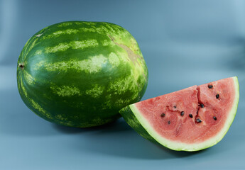 A whole watermelon and a slice with a crack on a gray background. The concept is an overripe watermelon.
