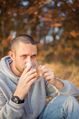 Portrait of a young handsome bearded man with a cup of tea on a picnic. Autumn concept.