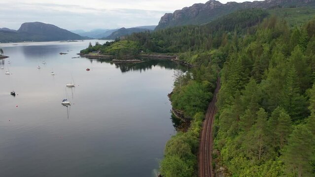 Magical drone shot of Plockton harbour at sunset. The shot sweeps along the train track and waters edge and opens up into the main harbour.